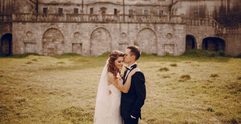 Groom kissing his wife's forehead with stone building background