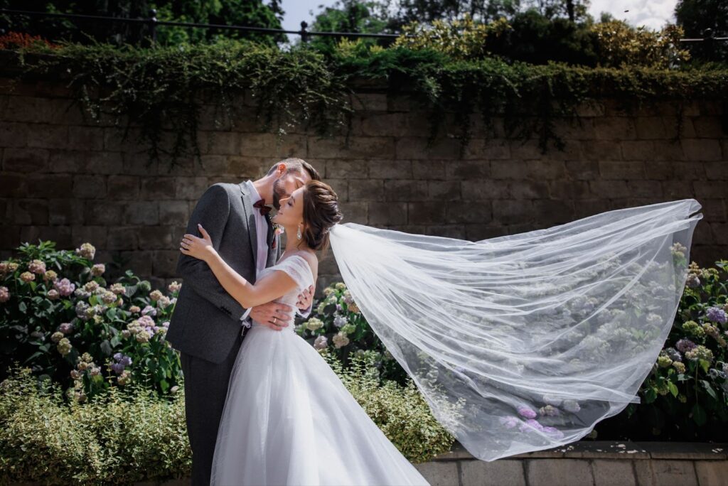 Wedding couple is kissing in the garden full of tender flowers on the sunny day