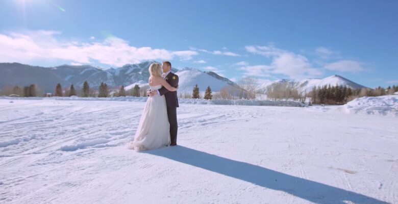 A couple embraces in a snowy landscape with mountains in the background