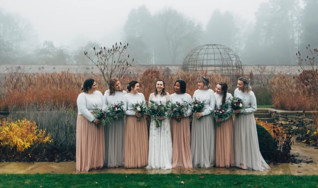 A bride and her bridesmaids stand together in a misty garden