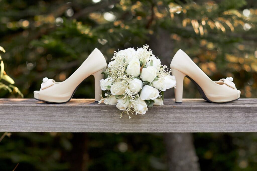 Wedding shoes and bouquet on a wooden railing with a blurred green background