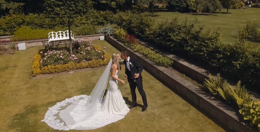 A couple sharing a kiss in a sunny garden with the bride's long veil spread out
