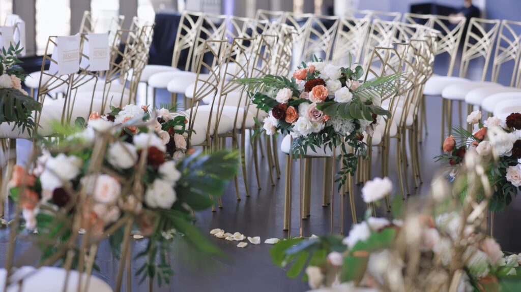 Chic wedding aisle flanked by flowers and modern gold chairs