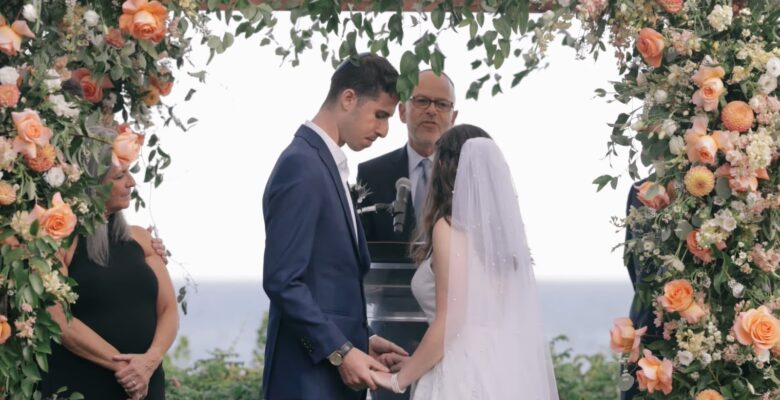 A couple exchanges vows under a floral archway